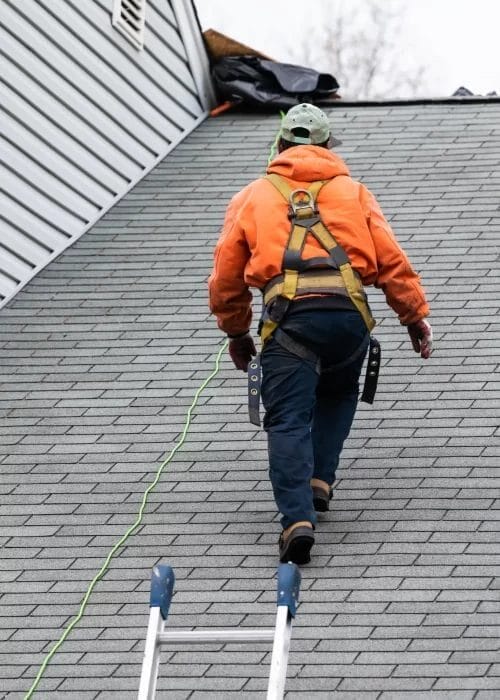 A roofer walking up a steep roof while wearing a safety harness.
