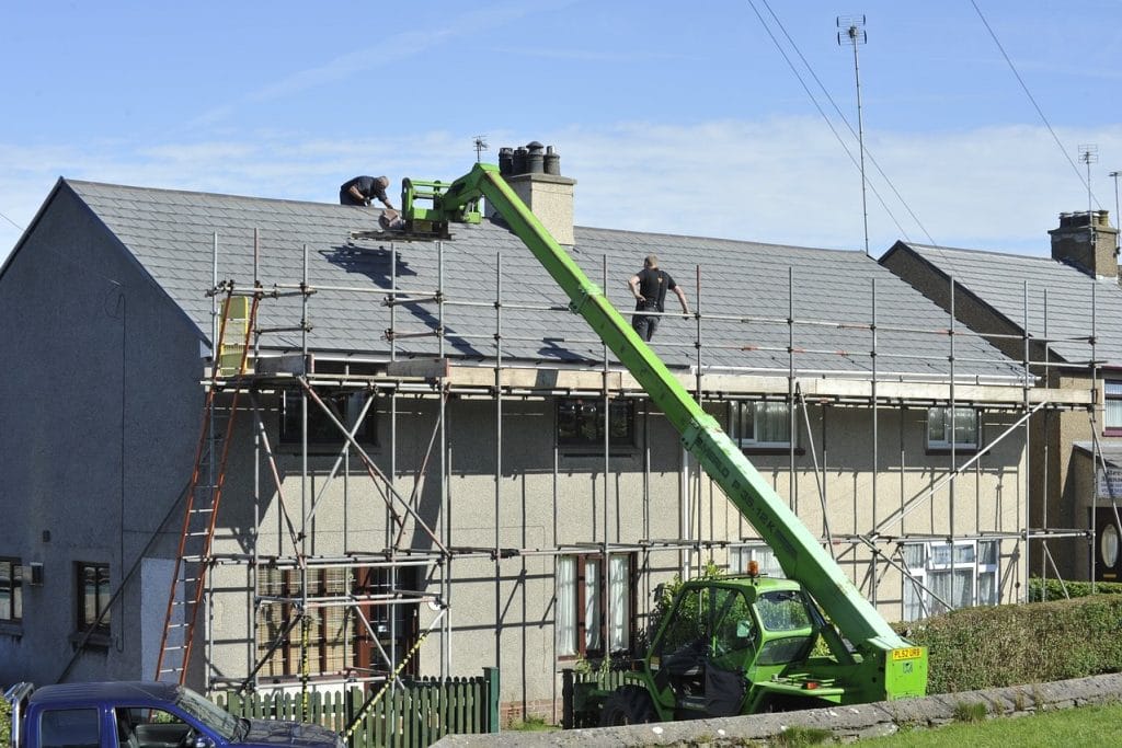 Roof repair in progress with workers on scaffolding using machinery