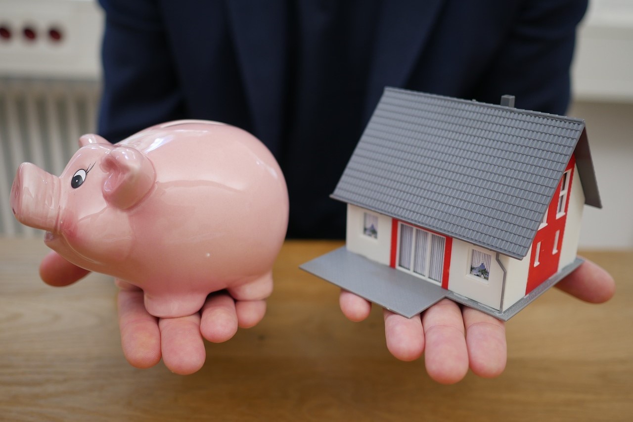 A person holding a piggy bank and model house, symbolizing financing options for homeownership.