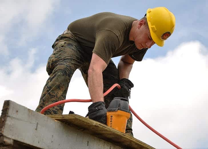 A contractor using a power tool on top of a roof