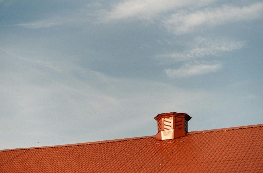 Vent on top of a red tin roof against the blue sky